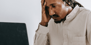 A stressed man looking at his screen with his hand to his face.