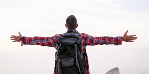 A man wearing a backpack with his hands spread out by his side looking into the horizon.