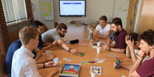 A group of men sat around a circle table playing Datopolis. 