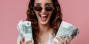 An excited woman holding cash in both hands.